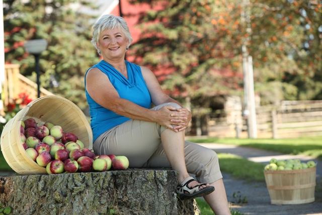 Cathy McKay sitting on a tree stump surrounded by apple baskets